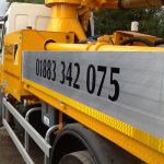 Closeup of Embassy Concrete Pumping phone number on side of truck-mounted concrete boom pump