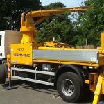 Side view of a Sermac concrete boom pump reaching over trees